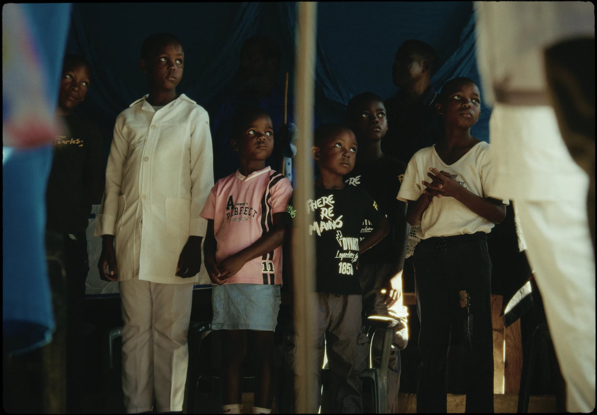 Un groupe d’enfants regarde vers l’extérieur d’une tente bleue.