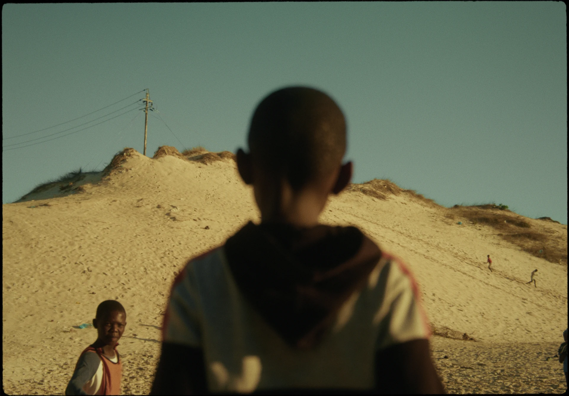 Des enfants jouent au pied d’une dune de sable.