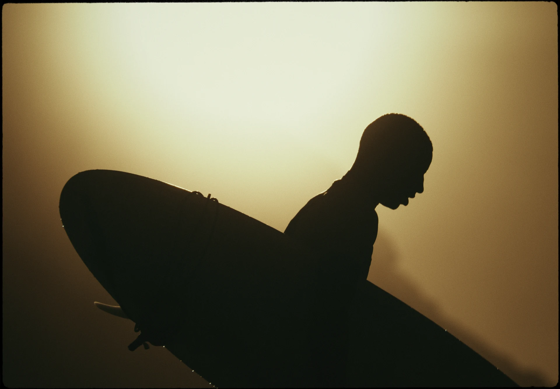 La silhouette d’un surfeur portant sa planche au soleil couchant.