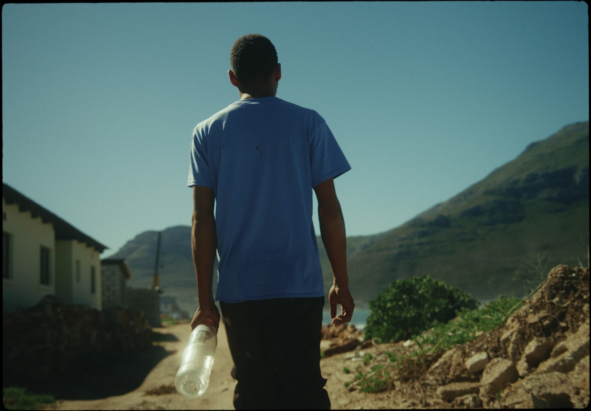 Un jeune homme marche avec un bidon dans un village.