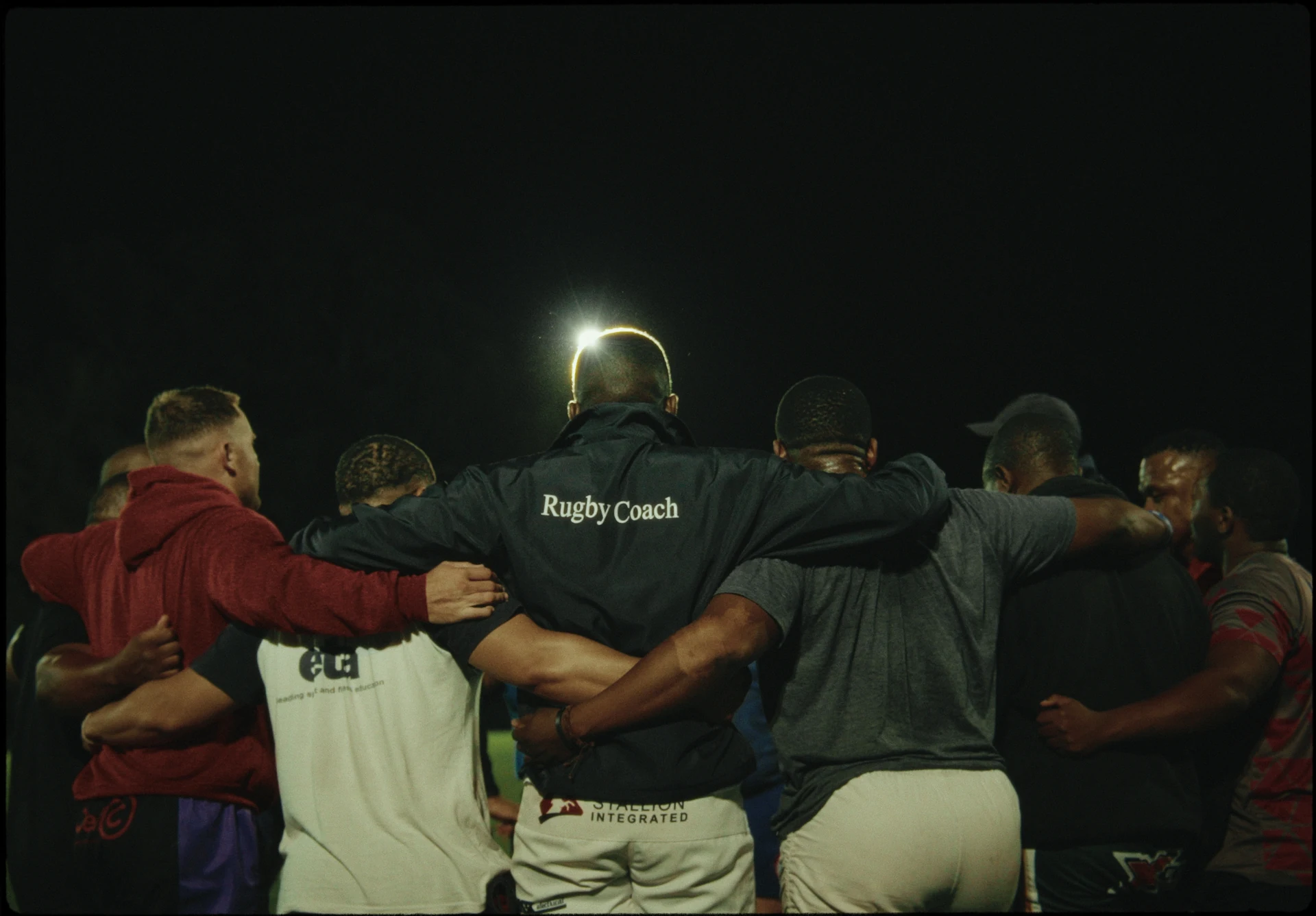 Des joueurs de rugby se rassemblent, les bras autour des épaules.